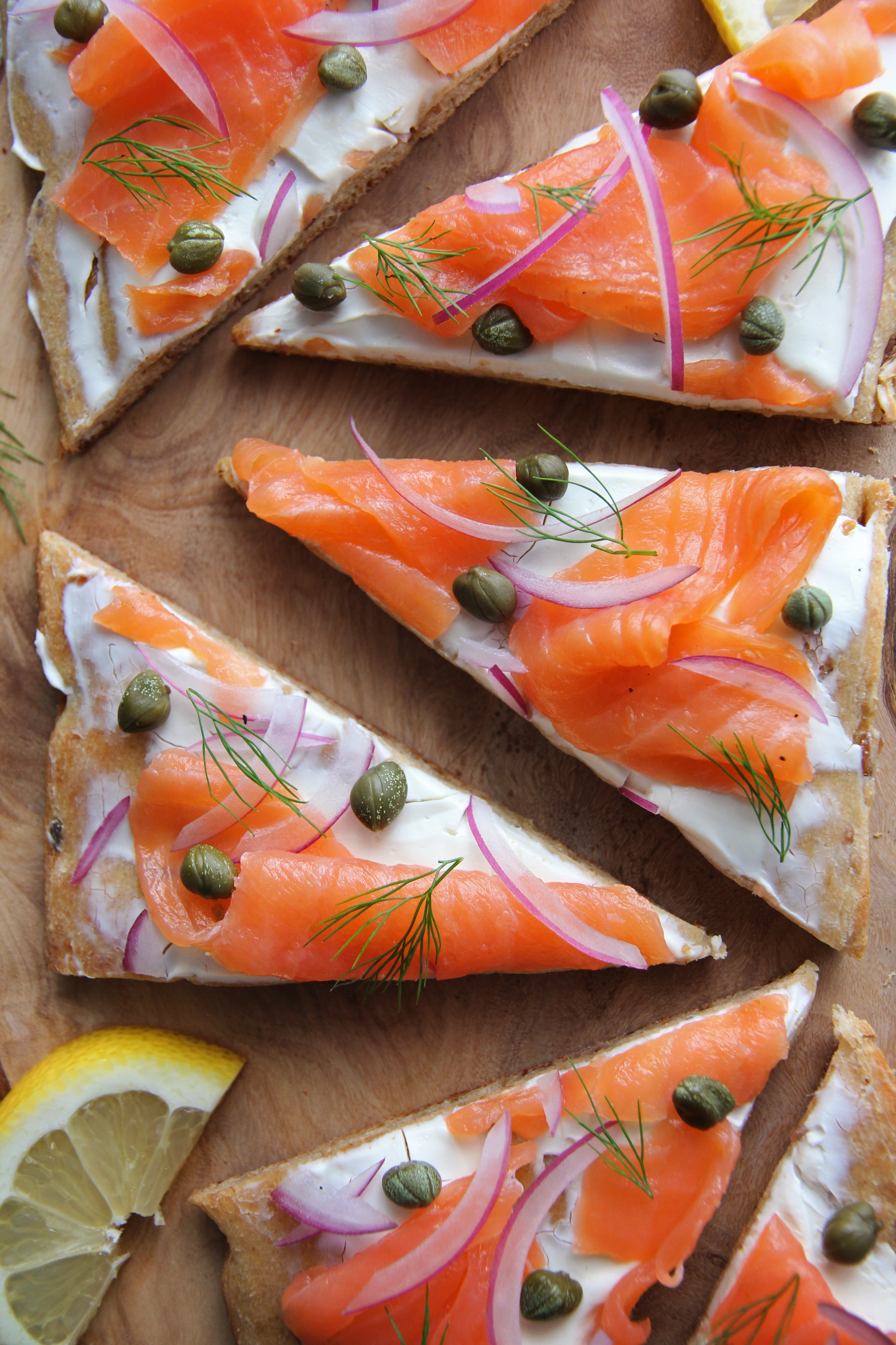 overhead image of smoked salmon flatbread cut into triangles, garnished with red onion and capers. 