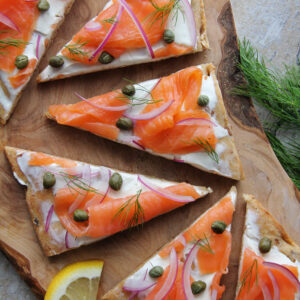 overhead image of smoked salmon flatbread cut into triangles, garnished with red onion, fresh dill and capers.