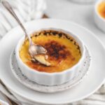 Bowl of easy creme brulee, resting on two white plates. A spoon is in the creme brulee.