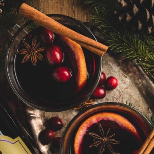 Overhead view of classic mulled wine mugs. Each mug is garnished with fresh cranberries, star of anise, orange slices and cinnamon sticks.