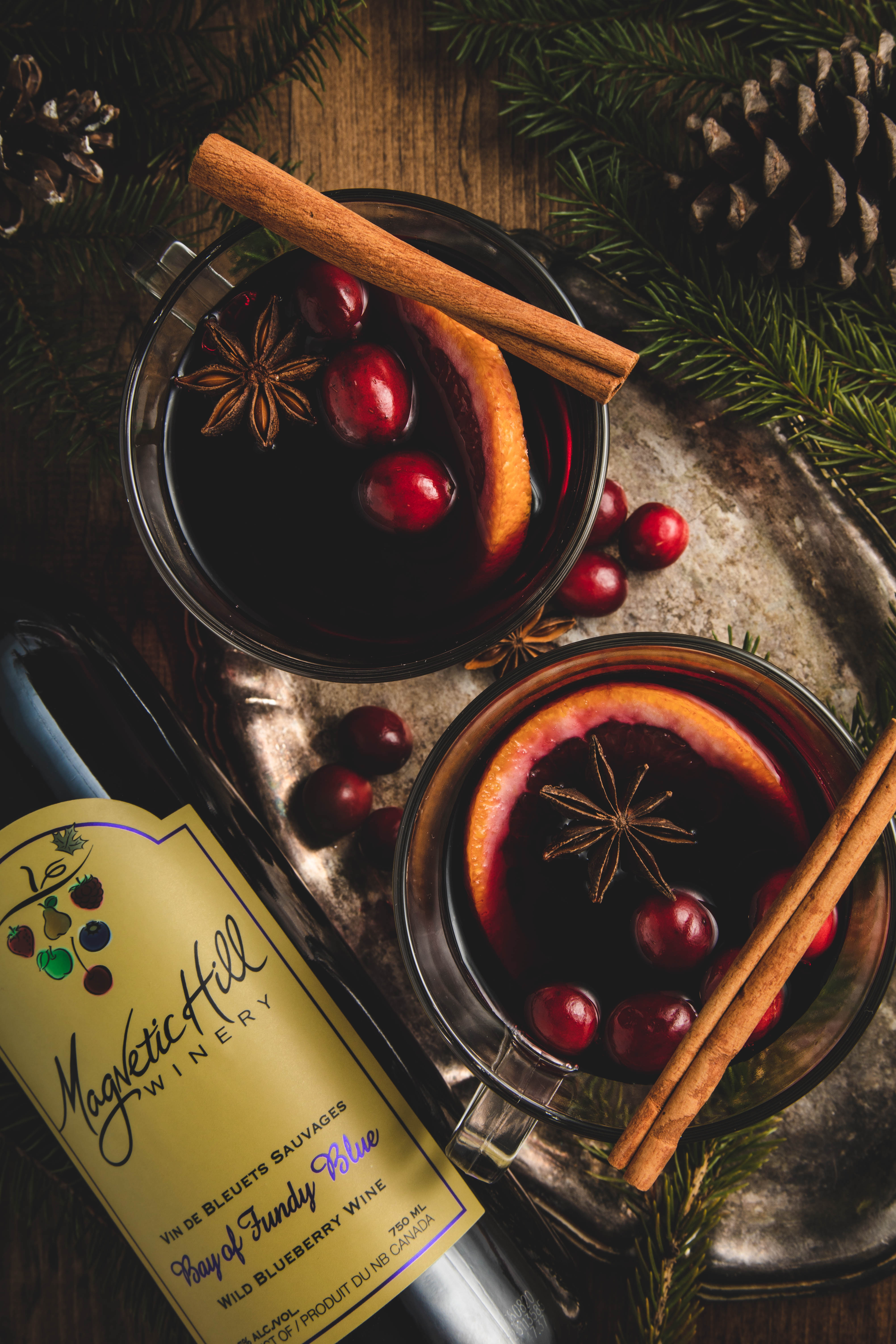 overhead image of two mulled wine glasses garnished with cinnamon sticks and star of anise with bottle of Magnetic Hill Winery