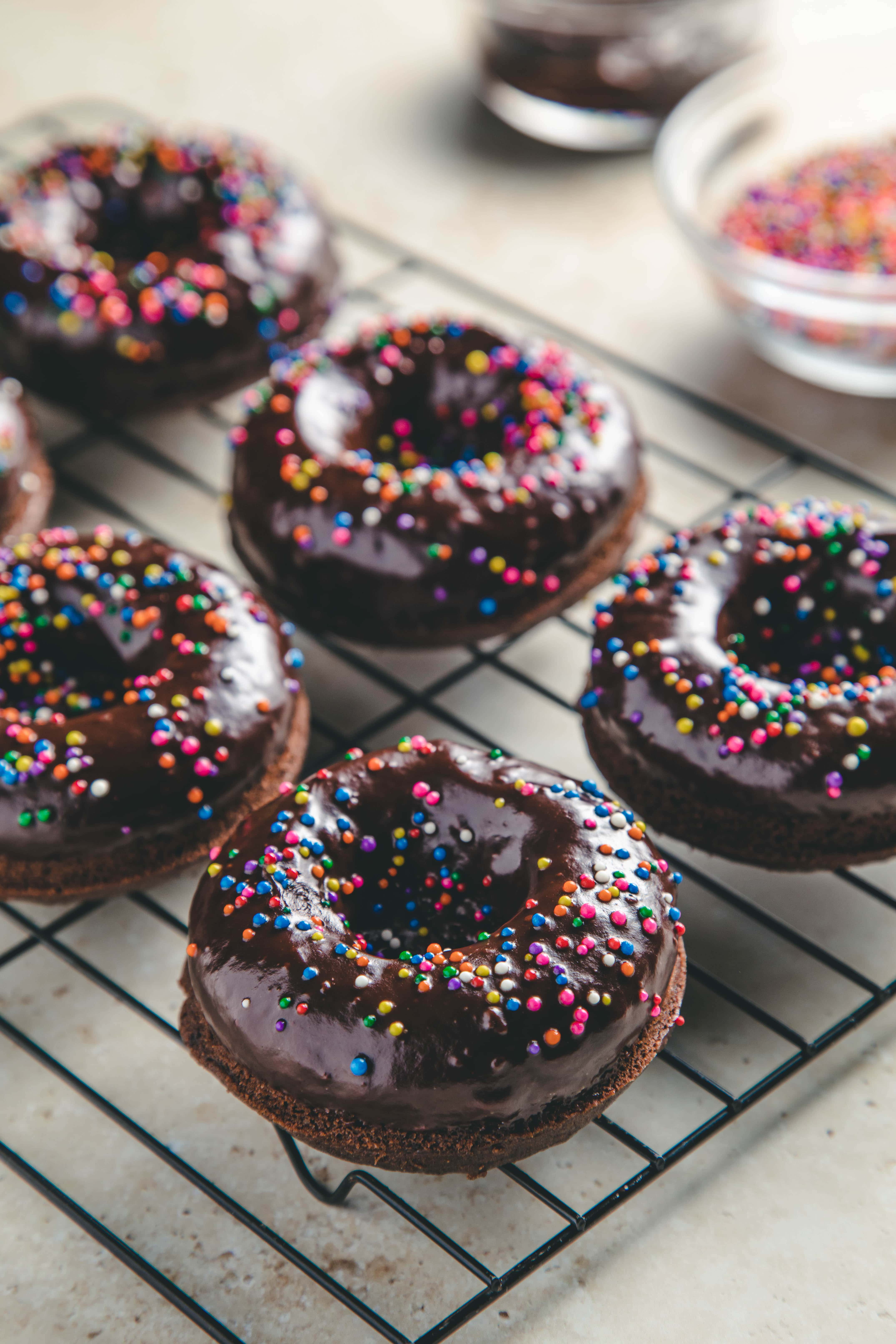 Baked double chocolate donuts with rainbow sprinkles on a cooling rack.