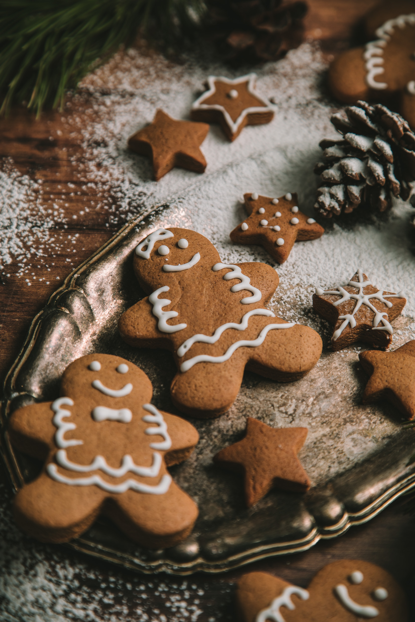 Overhead view of two gingerbread men cookies, decorated with white frosting and surrounded by star shaped gingerbread cookies and icing sugar.
