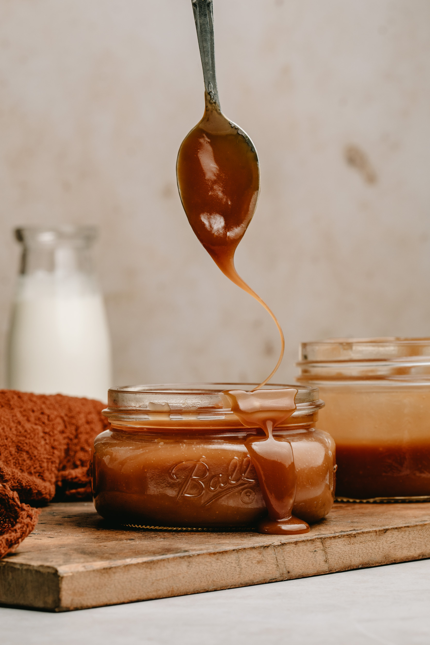 Drizzling 5 minute caramel sauce over a jar with a spoon.