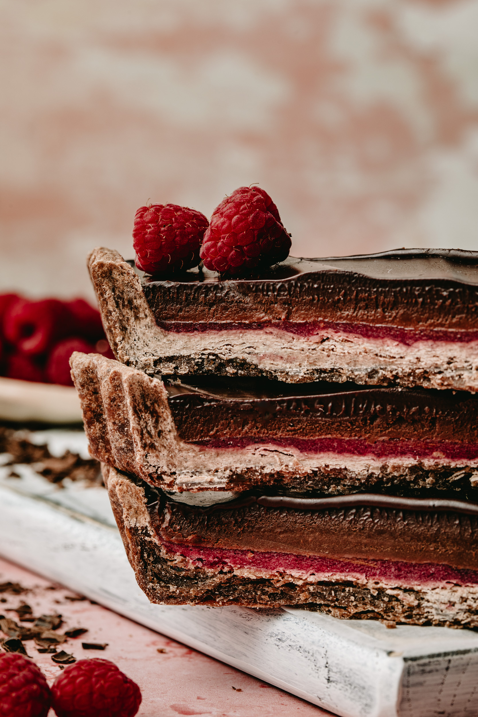 Stack of three slices of dark chocolate raspberry tart, garnished with fresh berries.