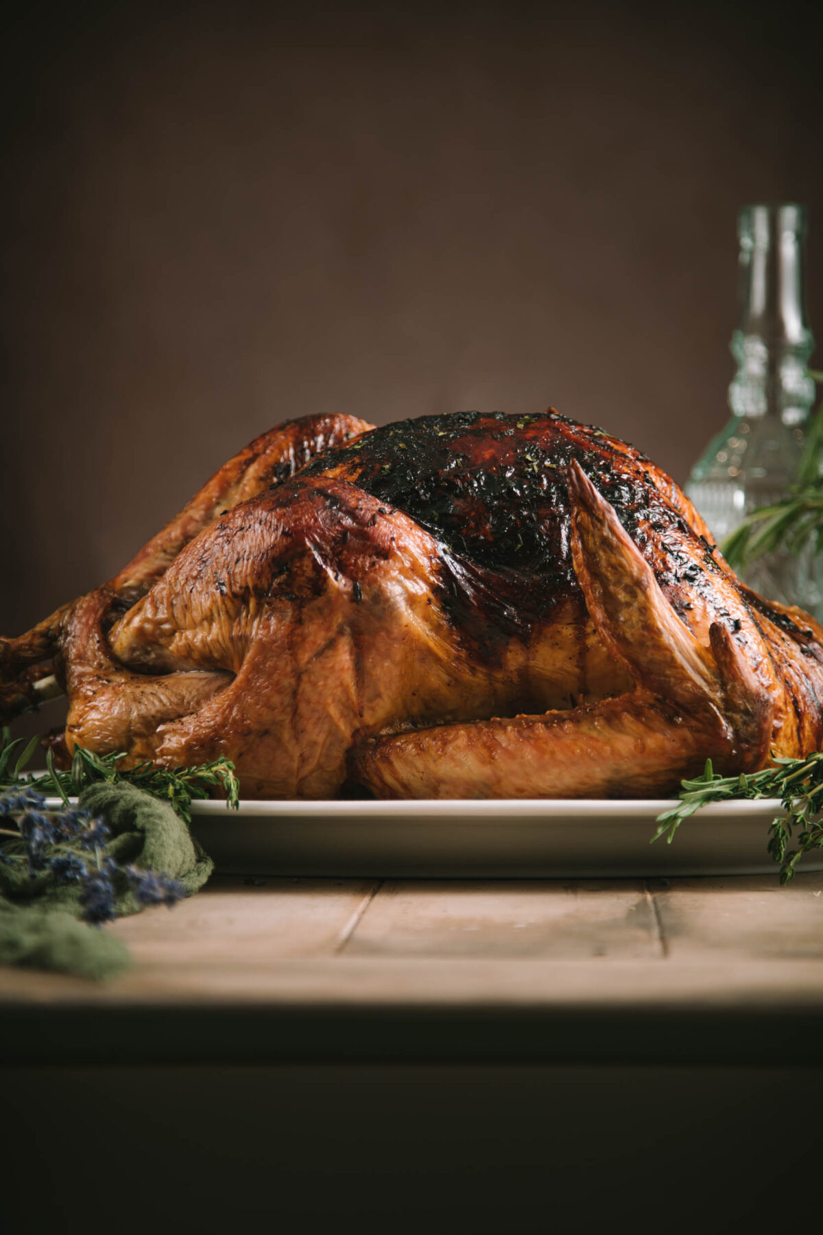 Fully cooked lavender honey turkey on a while serving plate, surrounded by fresh herbs.