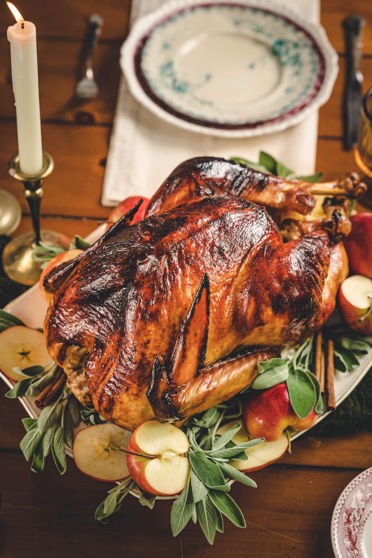 Whole roasted turkey, placed on a platter overtop sage leaves and surrounded by red apples.